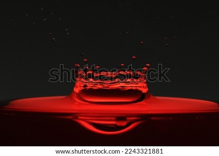 A drop of red water forming a coronet as it splashes into a glass full of liquid, backlit for contrast.