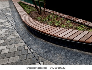 drop shaped or ellipse bench on cobbled square. the paneling of  bench seating area is made of tropical teak wood with great resistance to wind and rain. multi stemed tree and ornamental grases