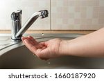A drop of water drips from faucet in human palm above round metal kitchen sink
