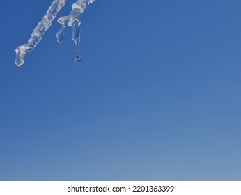 A Drop Of Water Dropping From A Melting Icicle With A Deep Blue Sky As A Background.