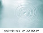 Drop of water falling into water with ripples and a blurred background