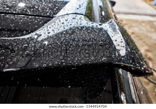Droplet on the car spoiler & windshield.\
Water beading after car wash or rain on shiny black\
 paint\
surface. Hydrophobic effect created by ceramic coat or paint\
sealant . Water drop\
Backgroud.