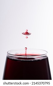Droplet of red wine falling in a glass isolated on white close up