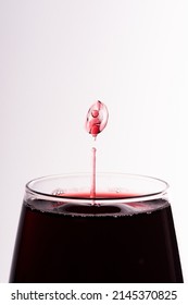Droplet of red wine falling in a glass isolated on white close up