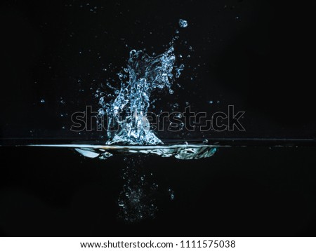 Droplet of water dropped into liquid and photographed while making splash on surface. Water splash isolated on dark background. Explosion on the water surface, abstract backgrond. Plash of liquid