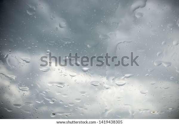 Droplets of rain on\
windscreen. Dark stormy sky behind the glass. Slightly dark\
vignetting on corners.