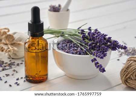 Dropper bottle of essential lavender oil, mortar of dry lavender flowers and sachets on white wooden table. 