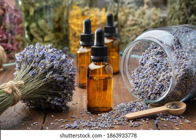Dropper bottle of lavender essential oil, glass jar of dry lavender flowers, bunches of dry lavender. Jars of different dry medicinal herbs on background. Alternative medicine. - Shutterstock ID 1863933778