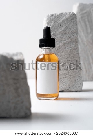 A dropper bottle mockup featuring a clean white label, placed on a white stone background in a minimalist and modern photography style. This image is perfect for cosmetic or skincare product mockups