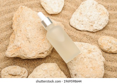 Dropper bottle of moisturizer, serum for face on stones with sand, sand background, summer face care