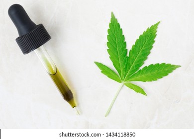 Dropper full of CBD oil and cannabis leaf viewed from above.
