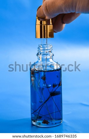Dropper glass Bottle Mock-Up. Oily drop falls from cosmetic pipette on blue background. Color of the year, close up dropper with Cannabis CBD Oil used for medical purposes.marijuana CBD oil on blue