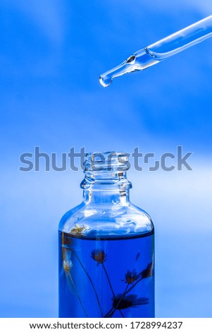 Dropper glass Bottle Mock-Up. Oily drop falls from cosmetic pipette on blue background. Color of the year, close up dropper with Cannabis CBD Oil used for medical purposes.marijuana CBD oil on blue