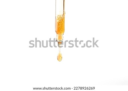 Dropper pipette with orange liquid drop on the whte isolated background. Oil, serum, acid cosmetic sample Close up.Copy space