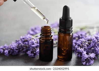 Dropping aromatherapy essential oil into a dark glass bottle, with fresh lavender flowers in the background - Powered by Shutterstock