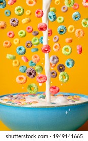 Dropping Cereals And Pouring Milk Into A Blue Bowl, Isolated On An Orange Background. Preparing Breakfast With Flying Colorful Cereals And Milk Drip.