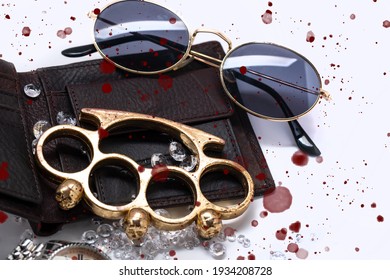 Drops Of Blood On Sunglasses And Brass Knuckles Watch Between Crystal Diamonds On Men's Wallet, Close Up, Selective Focus, Top View. The Concept Of Robbery, Looting And Mafia. Bloody Knuckle On White