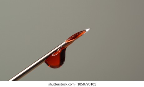 Drops of blood from the tip of the medical syringe. Bloody liquid dripping from needle, macro close up. Addiction horror illustration. Used syringe needle in blood. Administration of street drugs.