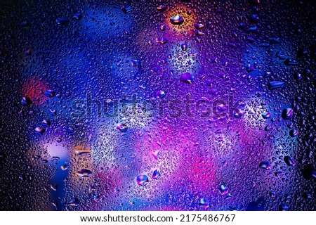 Drops of condensate on the sweaty glass. Cold foggy glass on background night lights.