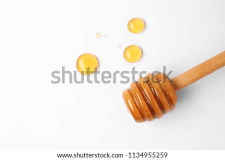 Drops of honey and dipper on white background, top view
