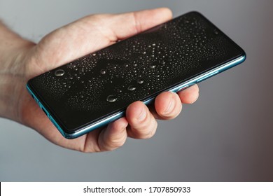 Drops on the glass of a smartphone screen, waterproof phone. man holds wet phone in his hand - Powered by Shutterstock