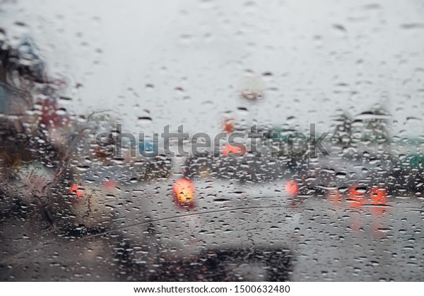 Drops Of\
Rain Drizzle on the glass windshield in the evening. street in the\
heavy rain. Bokeh Tail light and Traffic lights in city. Please\
drive  car carefully, slippery road. soft\
focus.