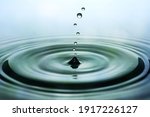 Drops of rain falling on smooth water surface. Green blurred pattern in background.