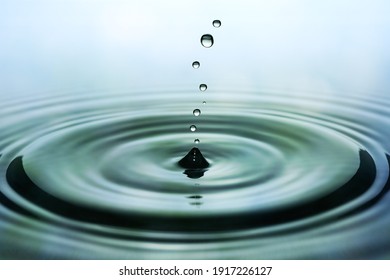 Drops Of Rain Falling On Smooth Water Surface. Green Blurred Pattern In Background.