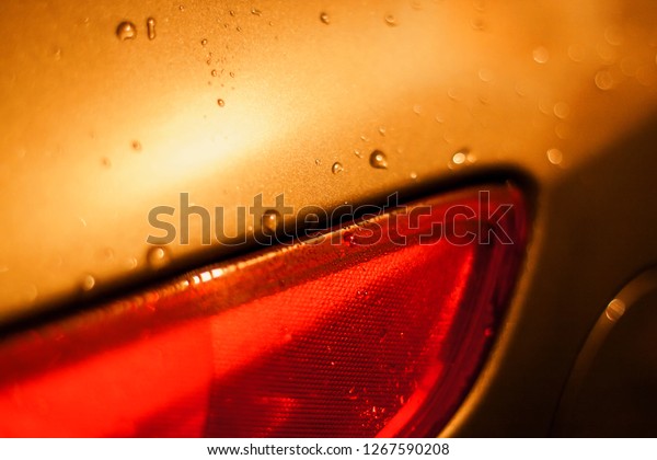 drops of a rain flow down on the\
smooth surface of gold metal and red plastic in easy\
sunlight