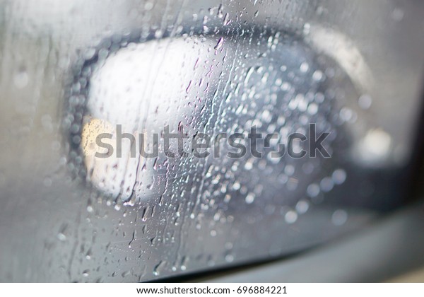 Drops of rain on the car\
window (glass) with a view of the exterior mirror and blurred\
background