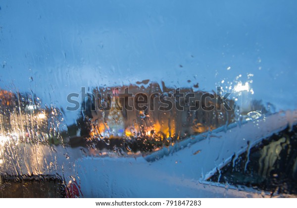 Drops of rain on the\
window of the car, the lights of the night city in blurring. Blurry\
car silhouette