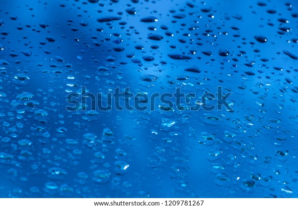 Drops of rain on the window glass. Shallow\
DOF. Window after rain. Blue Water background with water\
drops.\
ฺBright clear blue with incline camera\
angle.