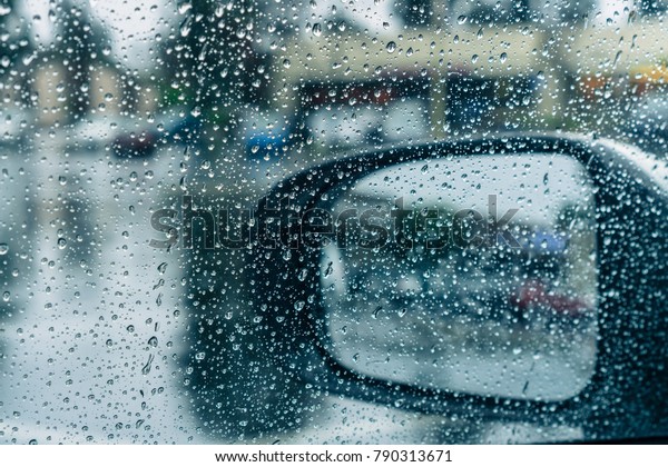 Drops of rain on the window and on the wing\
mirror; wet pavement in the\
background;