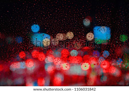 Drops Of Rain Water In Night Or Evening Street Lights On Red Glass Background. Street Bokeh Boke Lights Out Of Focus.