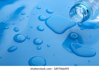 Drops of spilled water and plastic bottle on blue background, closeup