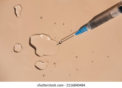 Drops of a transparent liquid and a sterile medical syringe on a beige background. Flat lay, place for text.