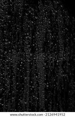 Drops of water flow down the surface of the clear glass on a black background. Vertical placement of the frame. Texture for creativity.