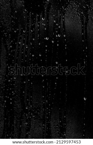 Drops of water flow down the surface of the clear glass on a black background. Vertical placement of the frame. Texture for creativity.