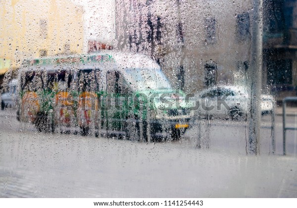 Drops of water flow down the windowpane.\
Waking the weather outside the window. Cars drive on a wet road.\
Abstract background