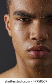 Drops of the water on face of a young man on black background.
