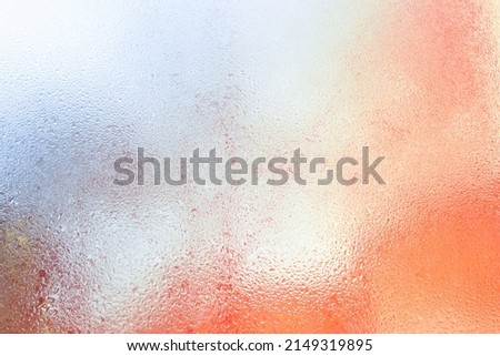 Drops of water on the glass. The fogged window. Background of frosted glass texture with orange contrasting illumination from the sun. A blurry view of the urban landscape.