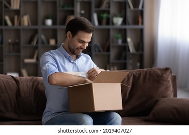 Dropshipping. Curious Young Guy Customer Sit On Couch Unbox Unpack Carton Container With Internet Order From Online Shop Store Marketplace. Happy Millennial Man Open Parcel Received By Courier Service