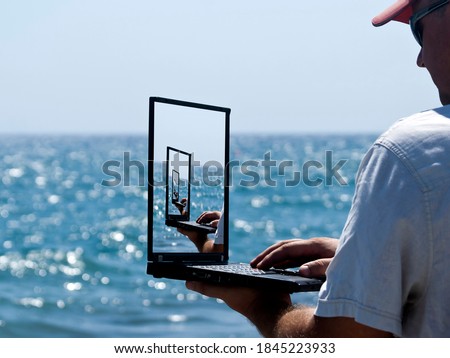 The Droste effect concept: Man using laptop in front of blue sea with picture recursively appearing within itself on computer monitor 