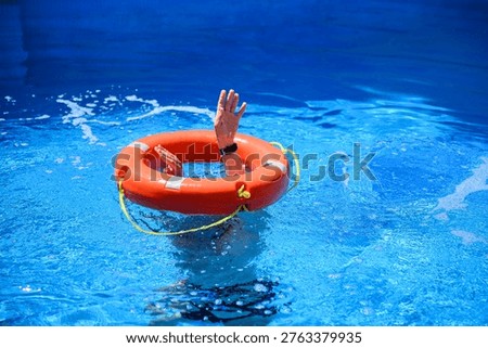 Drowning man in pool reaching out through lifebuoy. Concept of water rescue, emergency help, life saving. Orange life ring in water with person in distress needing assistance, emergency situation