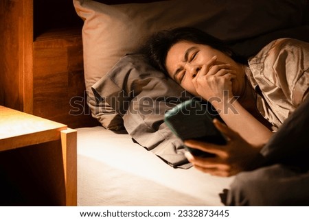 Drowsy woman lying in bed,addicted to her phone,constantly yawning,feeling tired,her heavy eyelids struggling to stay open,battled her sleepy state,symptoms of sleep procrastination or revenge bedtime