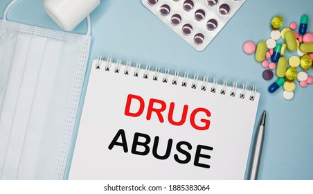 DRUG ABUSE Is Written In A Notebook On A Blue Background Next To Pills, Mask And Pen.