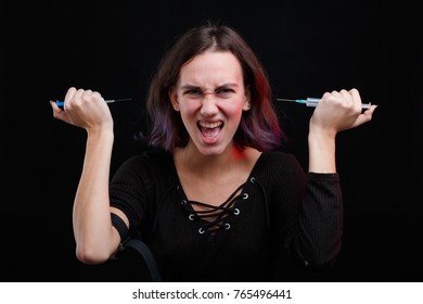 A drug addict holds two syringes in her hands and screams. On a black background. - Shutterstock ID 765496441