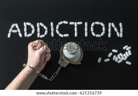 Drug addict or medical abuse concept with man handcuffed to a medicine bottle. Obsession to pharmaceutical substances or narcotics or anxiety pills. Addiction written with tablets on dark background.