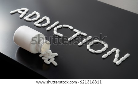 Drug addict or medical abuse concept. Obsession to pharmaceutical substances or narcotics or anxiety pills. Addiction written with white tablets. Medicine spilling out from a bottle on a dark table.