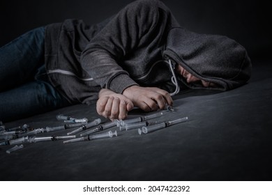 A drug addicted person draws a dose of the drug in a syringe. The guy is an addict, the concept of the fight against drugs. A young man sits in a pile of used syringes.